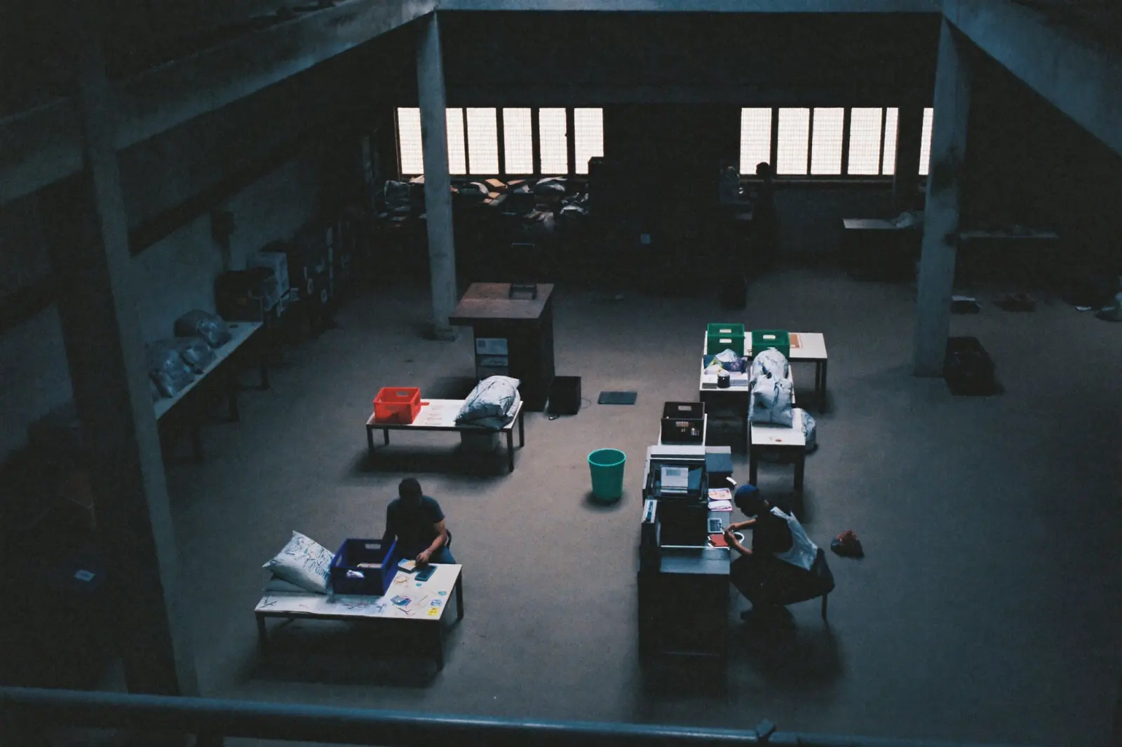 A large hall seen from a mezzanine, with staff at tables and crates under tall windows